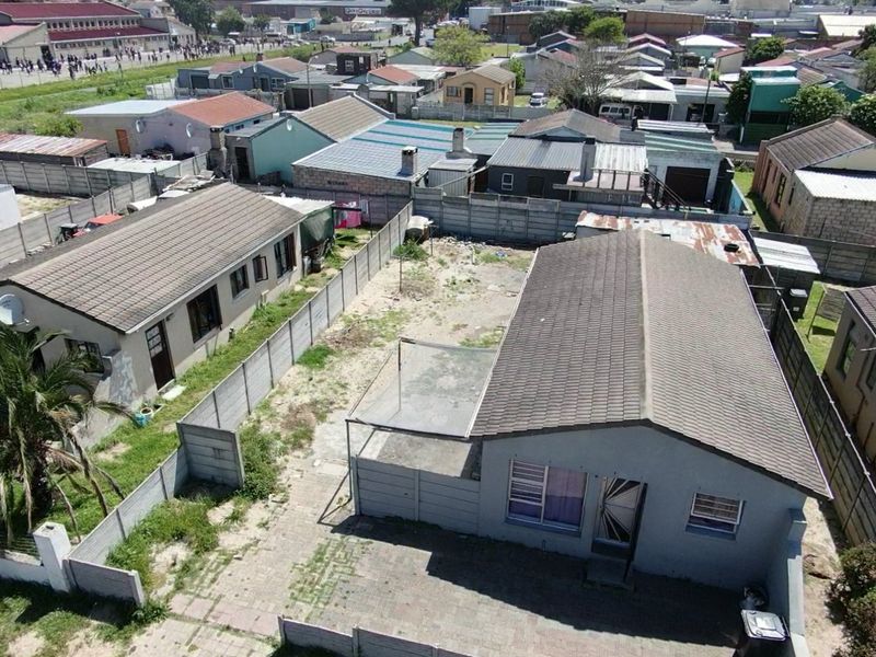 Aerial view of a residential property featuring a tiled roof house, paved driveway, and a large, unmaintained backyard enclosed by precast concrete walls.