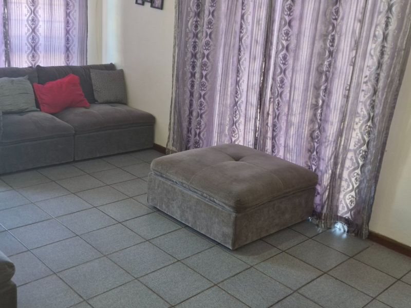 A living room area featuring tiled flooring and large sliding glass doors with curtains, providing access to the exterior.