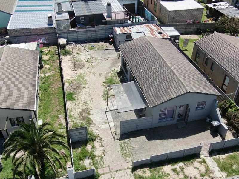 Aerial view of a residential property featuring a tiled roof house, paved driveway, and a large, unmaintained backyard with boundary walling.