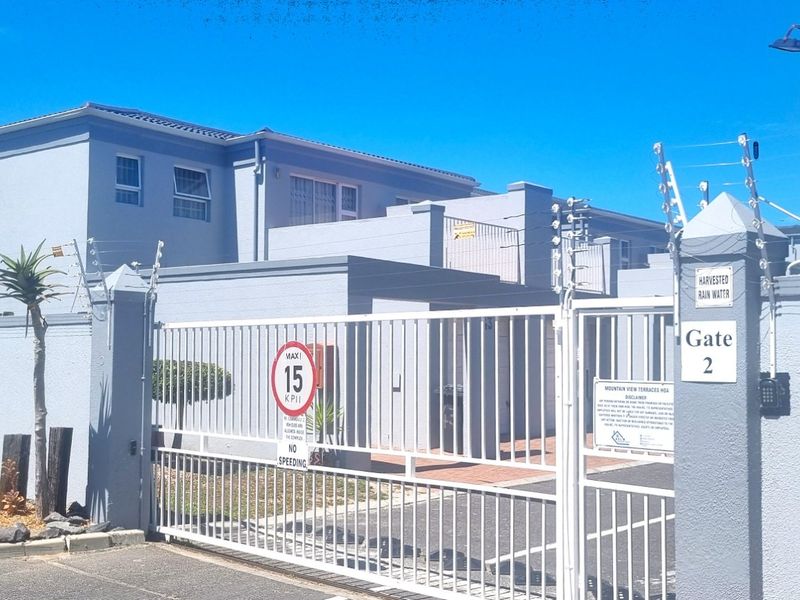 Front entrance view of the residential complex featuring a secure gated access point, perimeter wall with electric fencing, and external post boxes.