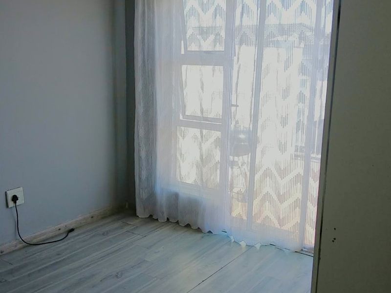 A bright, empty bedroom featuring modern laminate flooring and a large sliding glass door providing natural light and access to the exterior.