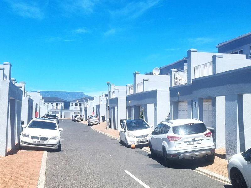 A street view of a residential complex featuring modern grey townhouses with paved driveways and garages.