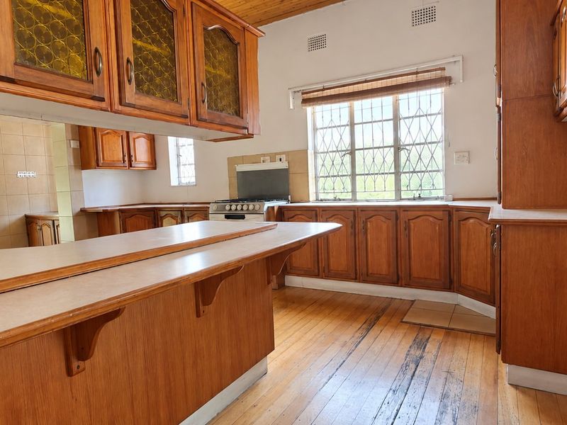A spacious kitchen featuring extensive wooden cabinetry, a breakfast bar, and timber flooring, offering a functional layout with potential for modern updates.