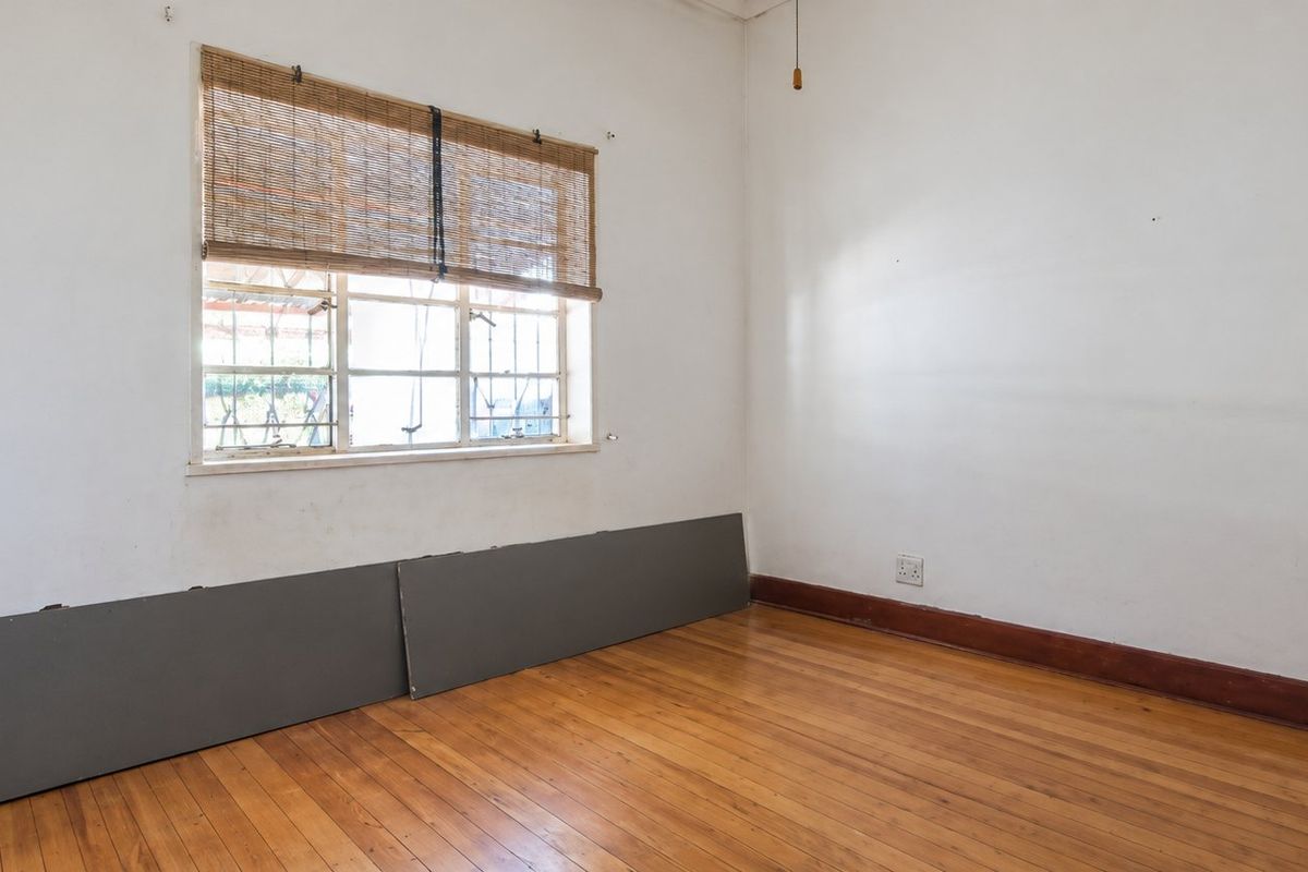 An empty bedroom featuring original timber flooring, a steel-framed window, and neutral walls, offering a blank canvas for renovation or interior design updates.