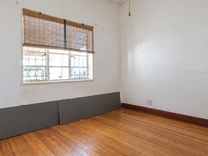 An empty bedroom featuring original timber flooring, a steel-framed window, and neutral walls, offering a blank canvas for renovation or interior design updates.