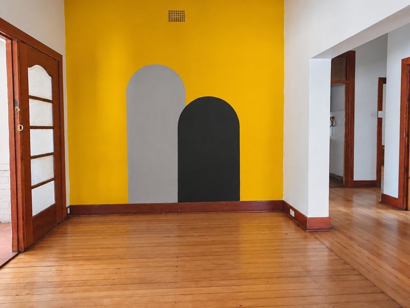 An empty living room featuring polished timber flooring, classic timber door frames, and a vibrant yellow accent wall with decorative arch motifs.