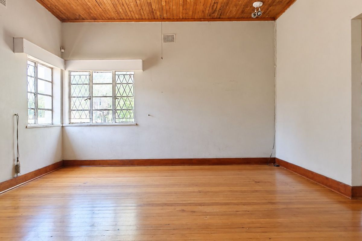 An empty living room featuring original timber flooring, a wood-paneled ceiling, and classic steel-framed windows, offering a blank canvas for renovation.