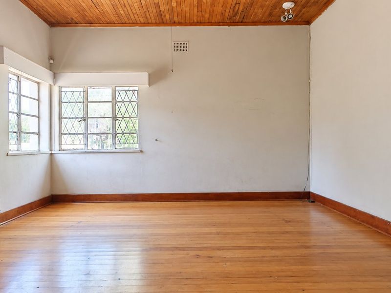 An empty living room featuring original timber flooring, a wood-paneled ceiling, and classic steel-framed windows, offering a blank canvas for renovation.