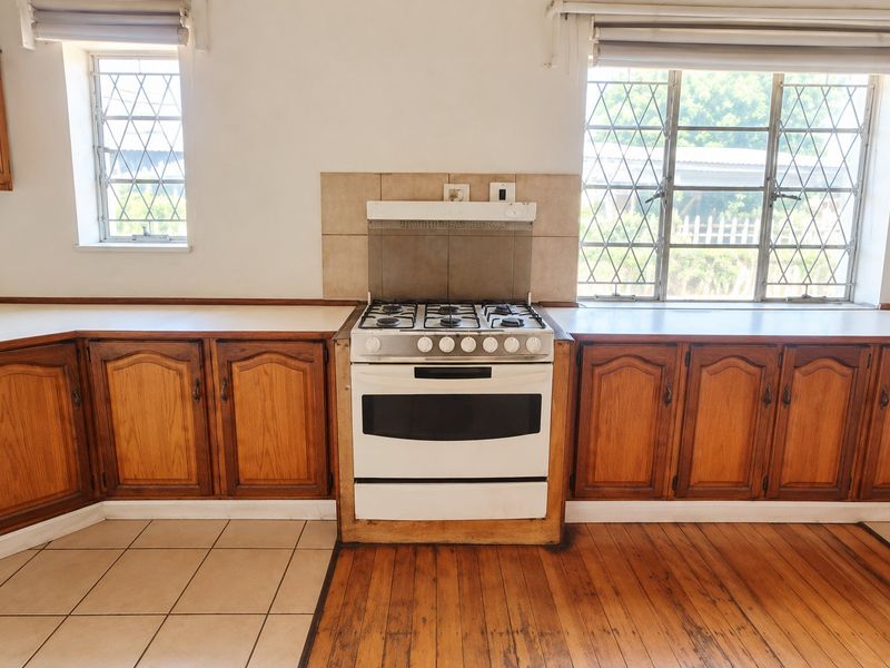 A functional kitchen featuring wooden cabinetry, a gas stove with extractor, and a mix of tiled and hardwood flooring with natural light.