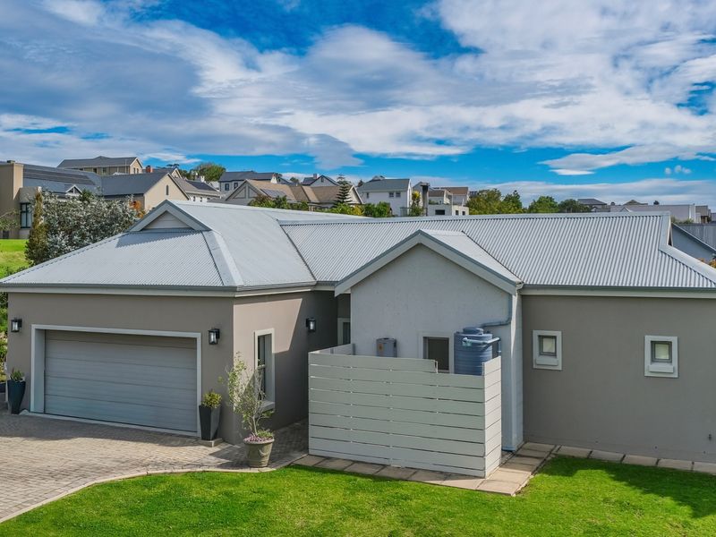 A well-maintained single-story home featuring a corrugated metal roof, double garage, paved driveway, and a private utility area with a water storage tank.