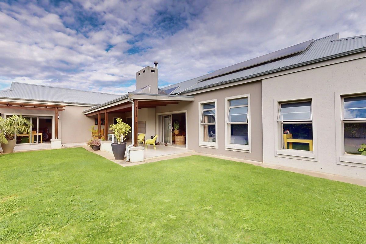 Rear view of the property featuring a covered patio, well-maintained lawn, solar panels, and modern exterior finishes.