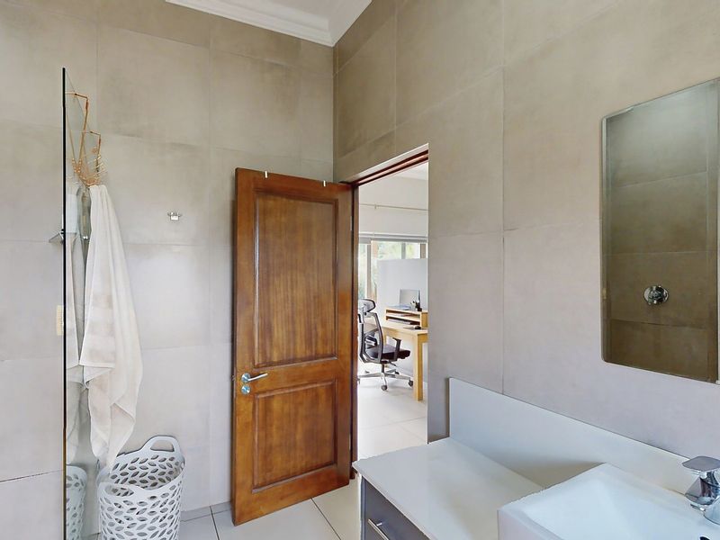 A modern bathroom featuring large format wall tiles, a vanity basin with chrome fixtures, and a glass shower screen.
