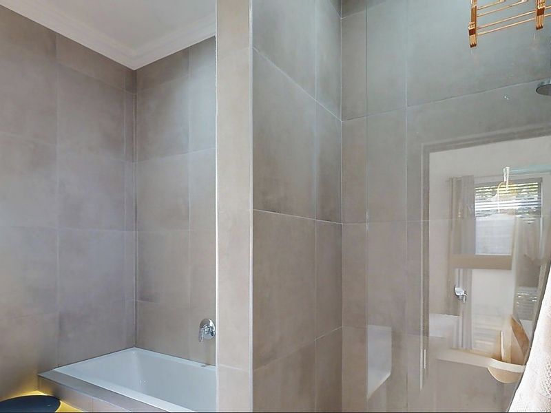 A modern bathroom featuring neutral wall tiles, a built-in bathtub, and a glass shower enclosure.