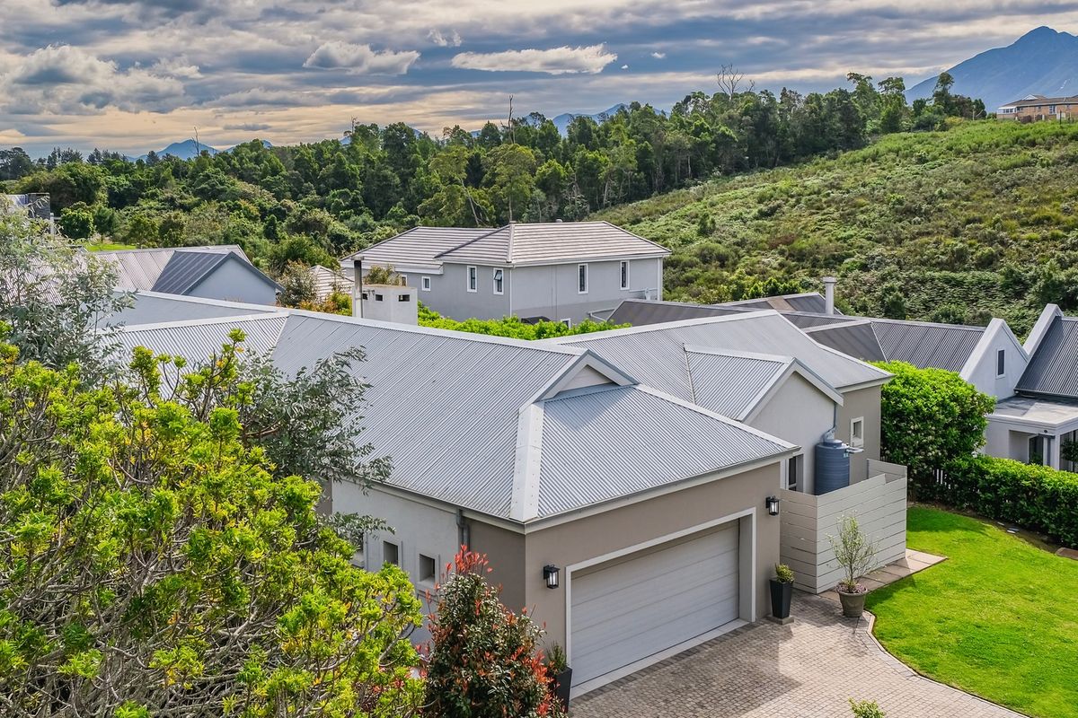 An aerial view of a residential property featuring a corrugated metal roof, paved driveway, and garage, set within a landscaped estate environment.