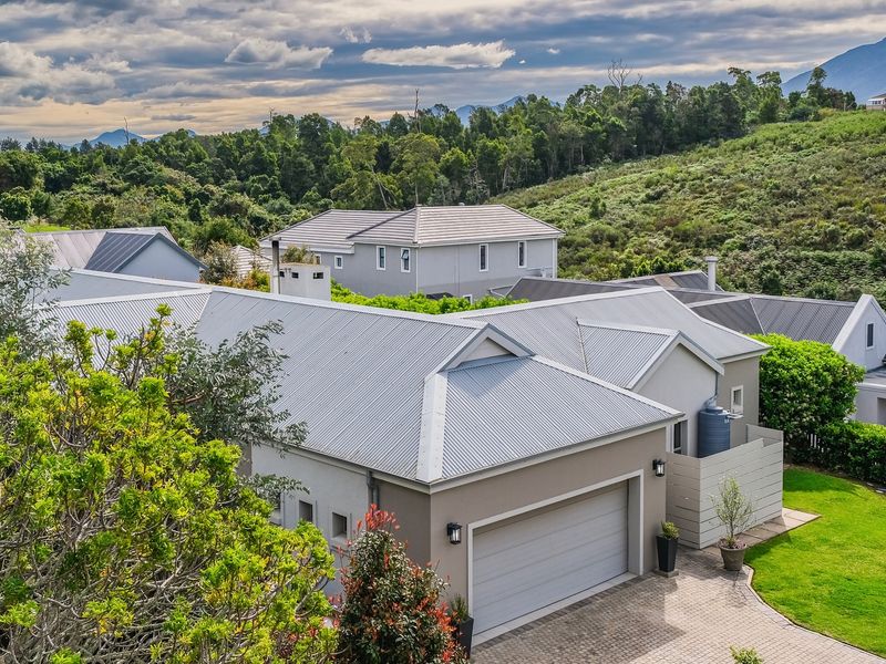 An aerial view of a residential property featuring a corrugated metal roof, paved driveway, and garage, set within a landscaped estate environment.