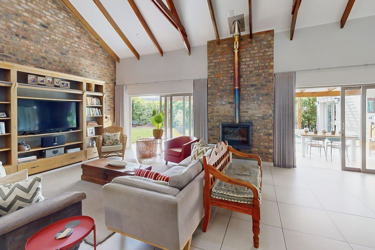 Spacious living room featuring vaulted ceilings with exposed timber beams, a prominent brick fireplace, and large sliding doors opening to the outdoor patio area.