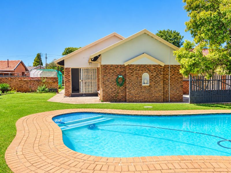 A well-maintained backyard featuring a swimming pool with brick paving, a face brick exterior facade, and a landscaped garden area.
