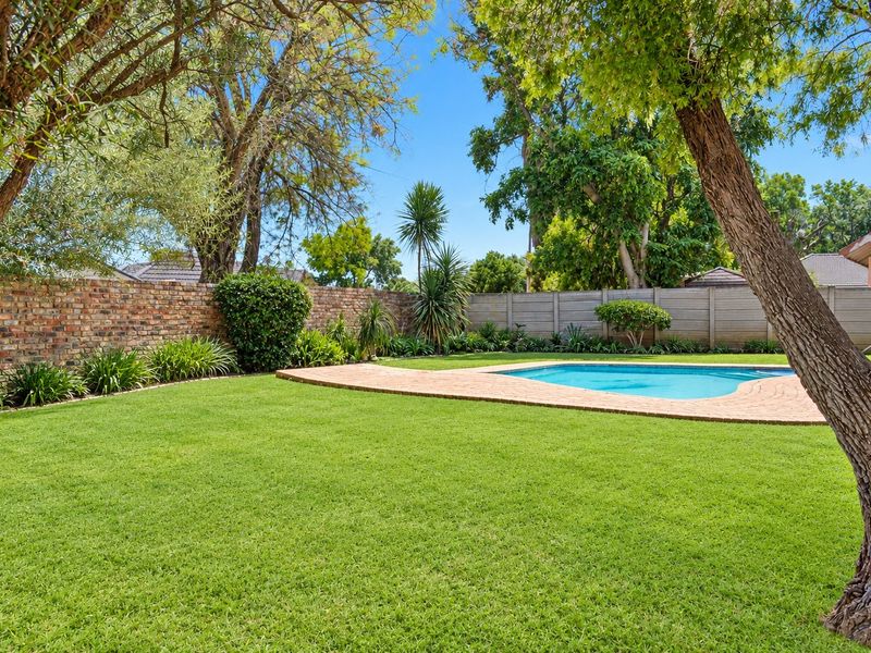 A well-maintained backyard featuring a swimming pool with a paved surround, lush green lawn, and established boundary walls.