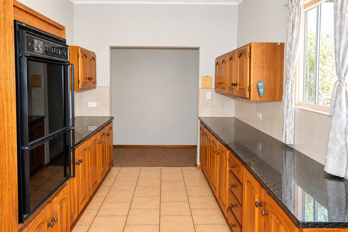 A functional kitchen featuring wooden cabinetry, granite countertops, a built-in double oven, and tiled flooring with a neutral backsplash.