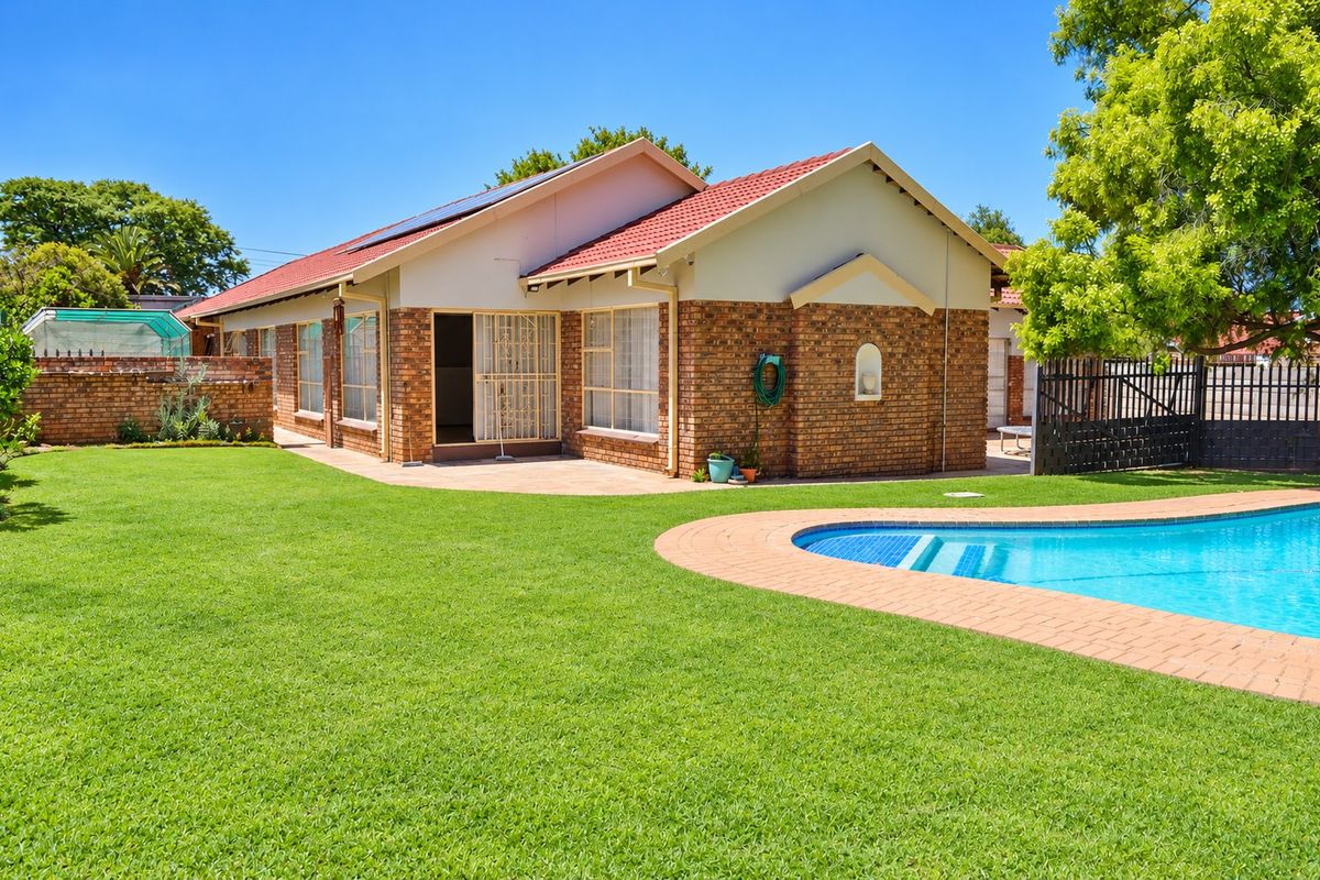 Rear view of the property featuring a well-maintained lawn, a swimming pool with paved surround, and a brick-faced house with solar panels.