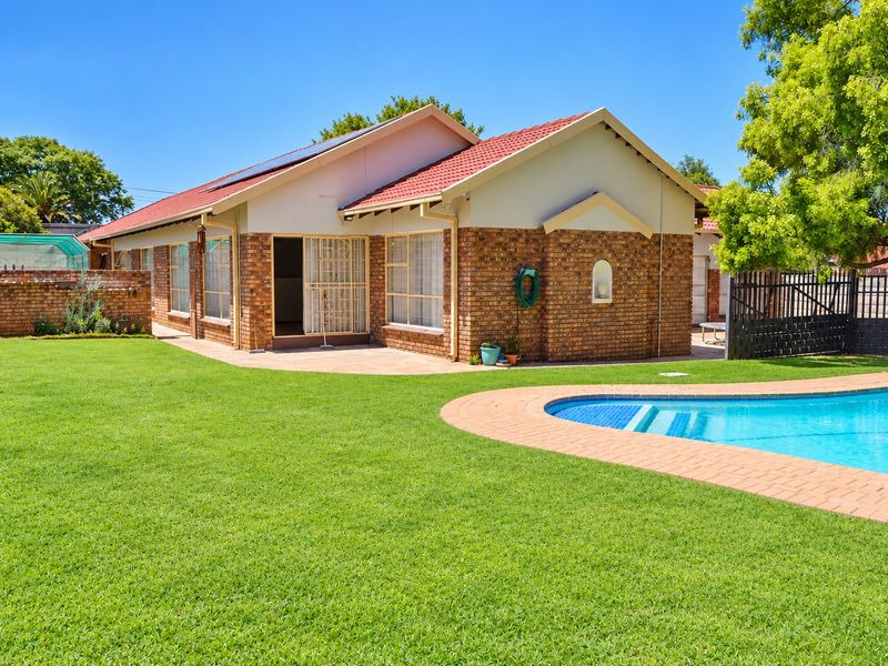 Rear view of the property featuring a well-maintained lawn, a swimming pool with paved surround, and a brick-faced house with solar panels.