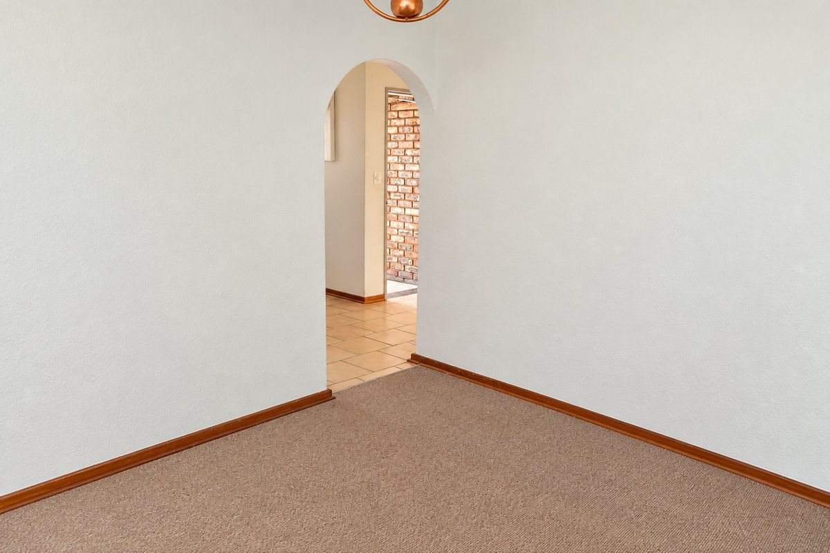 An empty living room featuring neutral carpeting, timber skirting boards, and a distinctive arched doorway leading to an adjacent tiled area.