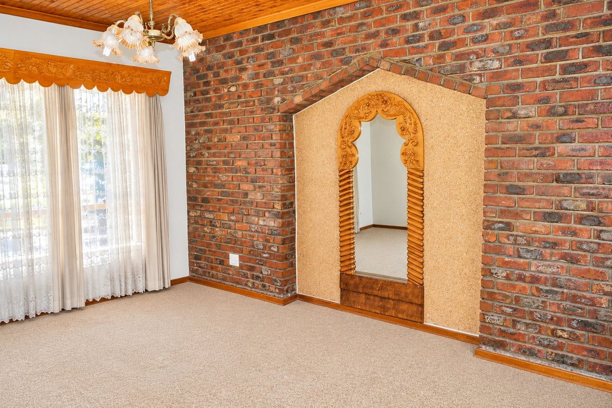 A spacious bedroom featuring an exposed brick wall, timber ceiling, and a unique built-in arched alcove with cork paneling.