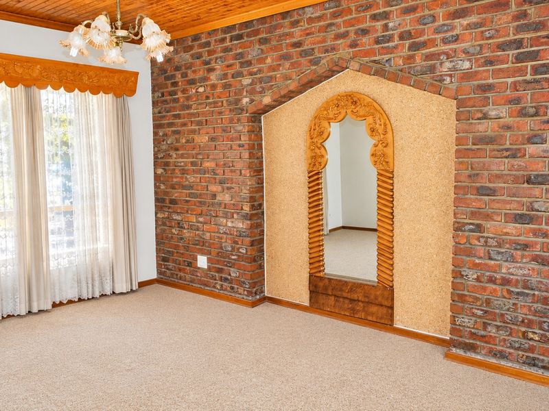A spacious bedroom featuring an exposed brick wall, timber ceiling, and a unique built-in arched alcove with cork paneling.