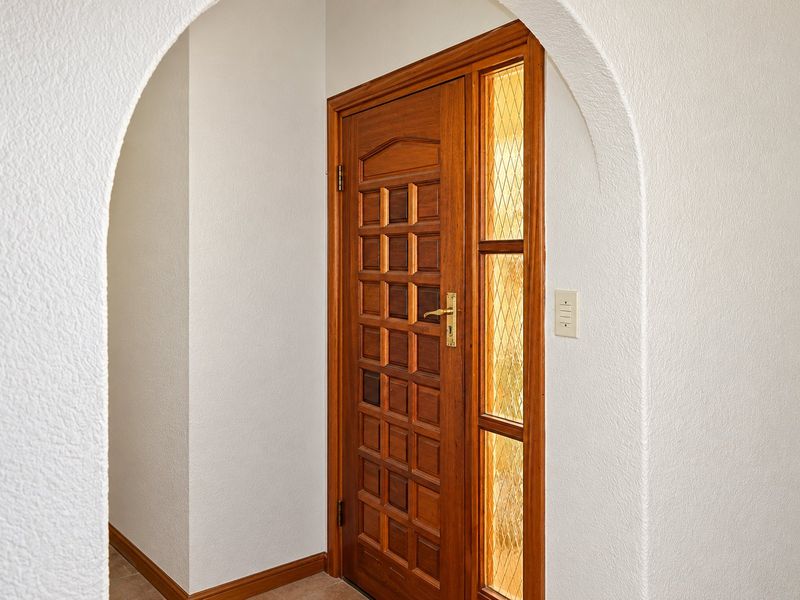 A welcoming entrance featuring a classic solid wood panel door with a decorative leaded glass sidelight, framed by a distinctive arched architectural opening.