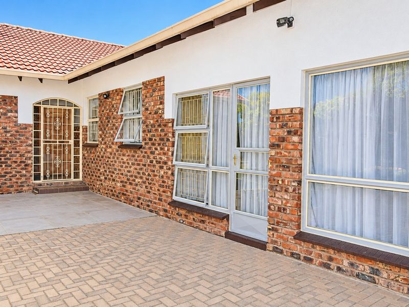 A well-maintained rear exterior view featuring a paved patio area, face brick facade, and secure aluminium window and door frames.