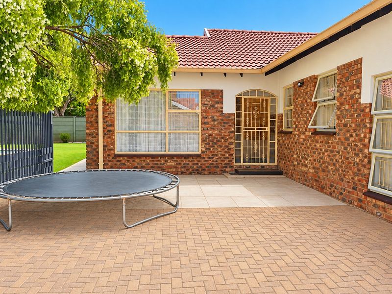 A well-maintained rear exterior featuring a paved patio area, classic brick facade, and secure window and door fixtures.