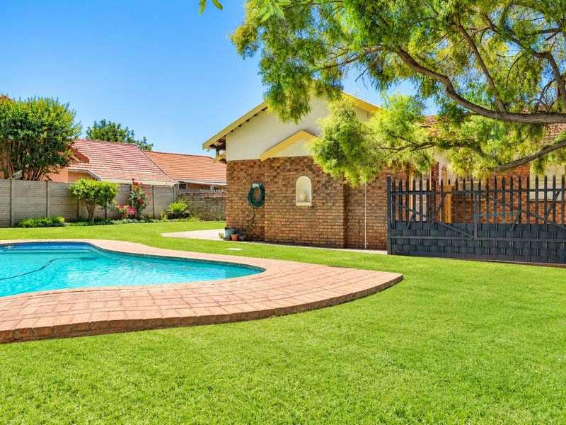 A well-maintained backyard featuring a swimming pool with brick coping, lush green lawn, and face brick exterior walling.