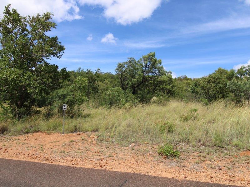 A view of a vacant residential plot featuring native vegetation and direct access from an asphalt road.