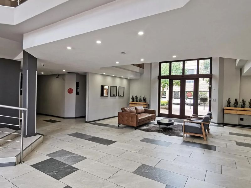 Spacious commercial building entrance lobby featuring modern tiled flooring, recessed lighting, and a prominent staircase with a stainless steel balustrade.
