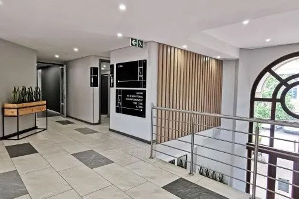 Modern commercial hallway featuring tiled flooring, timber slat wall detailing, stainless steel balustrades, and recessed ceiling lighting with clear directional signage.