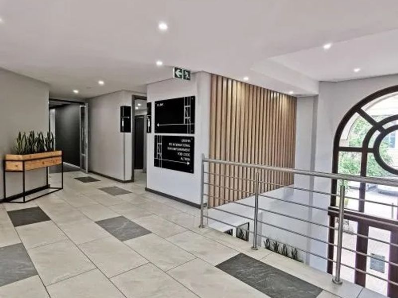 Modern commercial hallway featuring tiled flooring, timber slat wall detailing, stainless steel balustrades, and recessed ceiling lighting with clear directional signage.