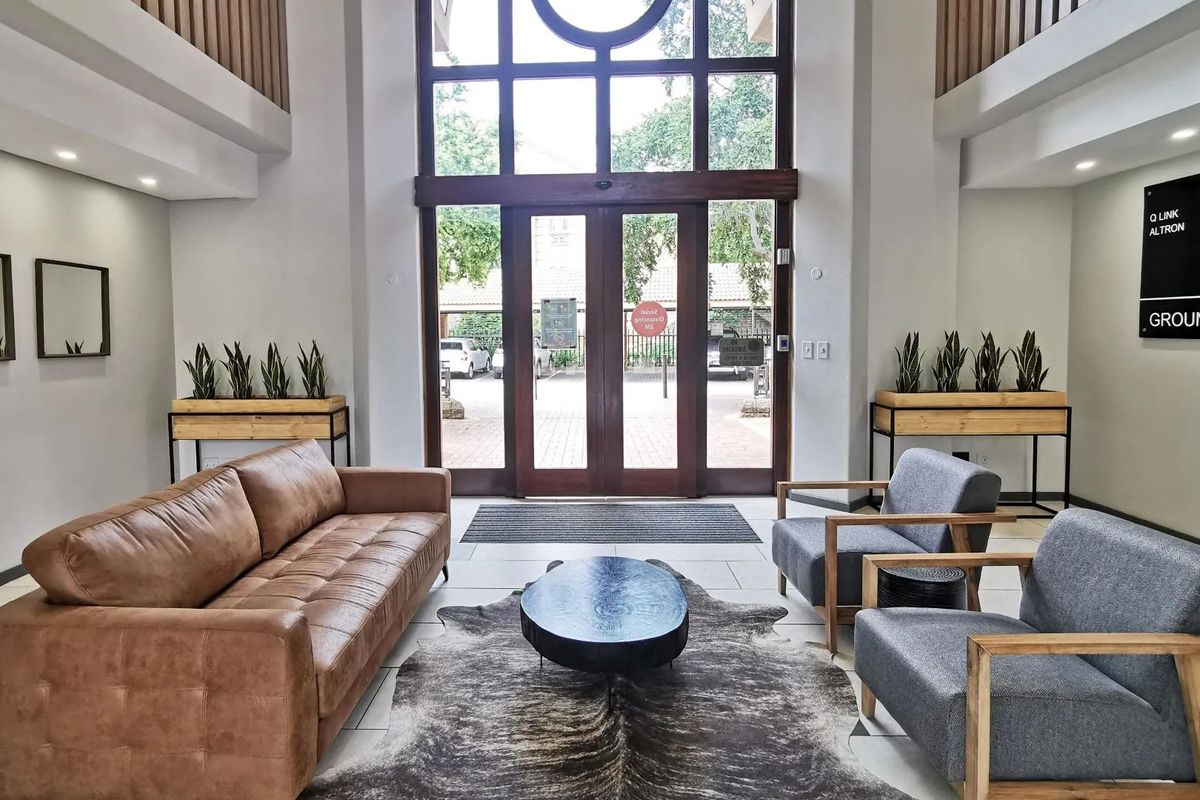 Spacious commercial building entrance lobby featuring double-height ceilings, large glass doors, and modern tiled flooring with a professional reception area aesthetic.