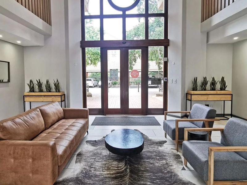 Spacious commercial building entrance lobby featuring double-height ceilings, large glass doors, and modern tiled flooring with a professional reception area aesthetic.