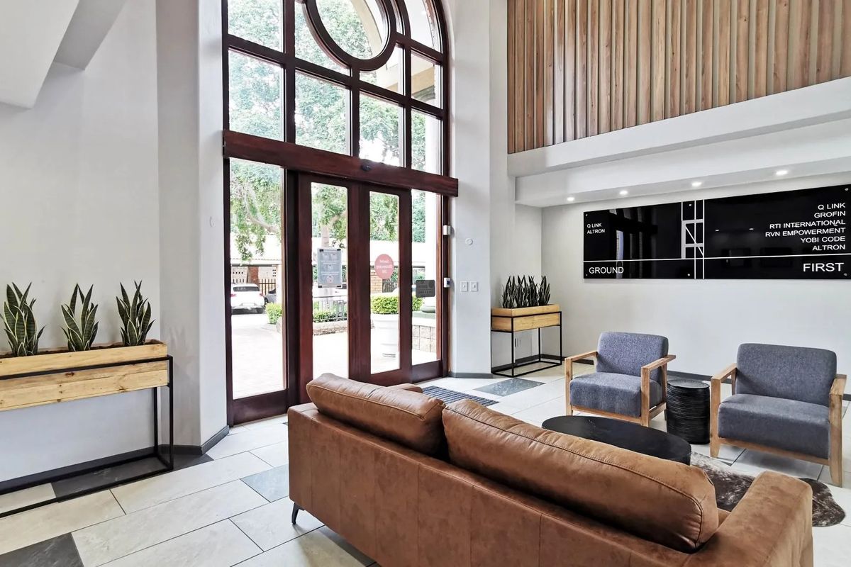 A bright and modern commercial entrance lobby featuring double-height arched glass doors, timber wall accents, and professional reception signage.
