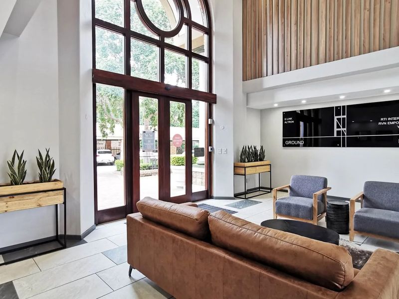 A bright and modern commercial entrance lobby featuring double-height arched glass doors, timber wall accents, and professional reception signage.