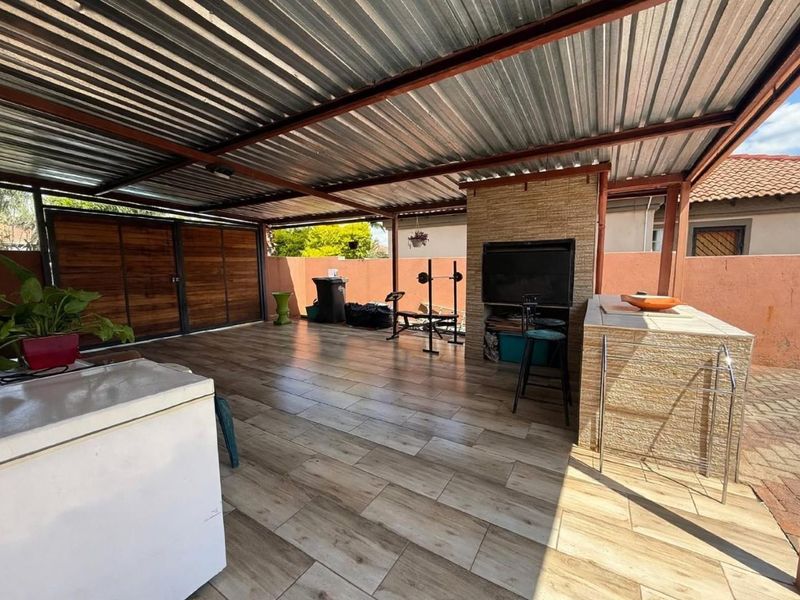 Covered outdoor patio area featuring a built-in braai, stone-clad counter, and durable tiled flooring, ideal for outdoor entertaining and relaxation.