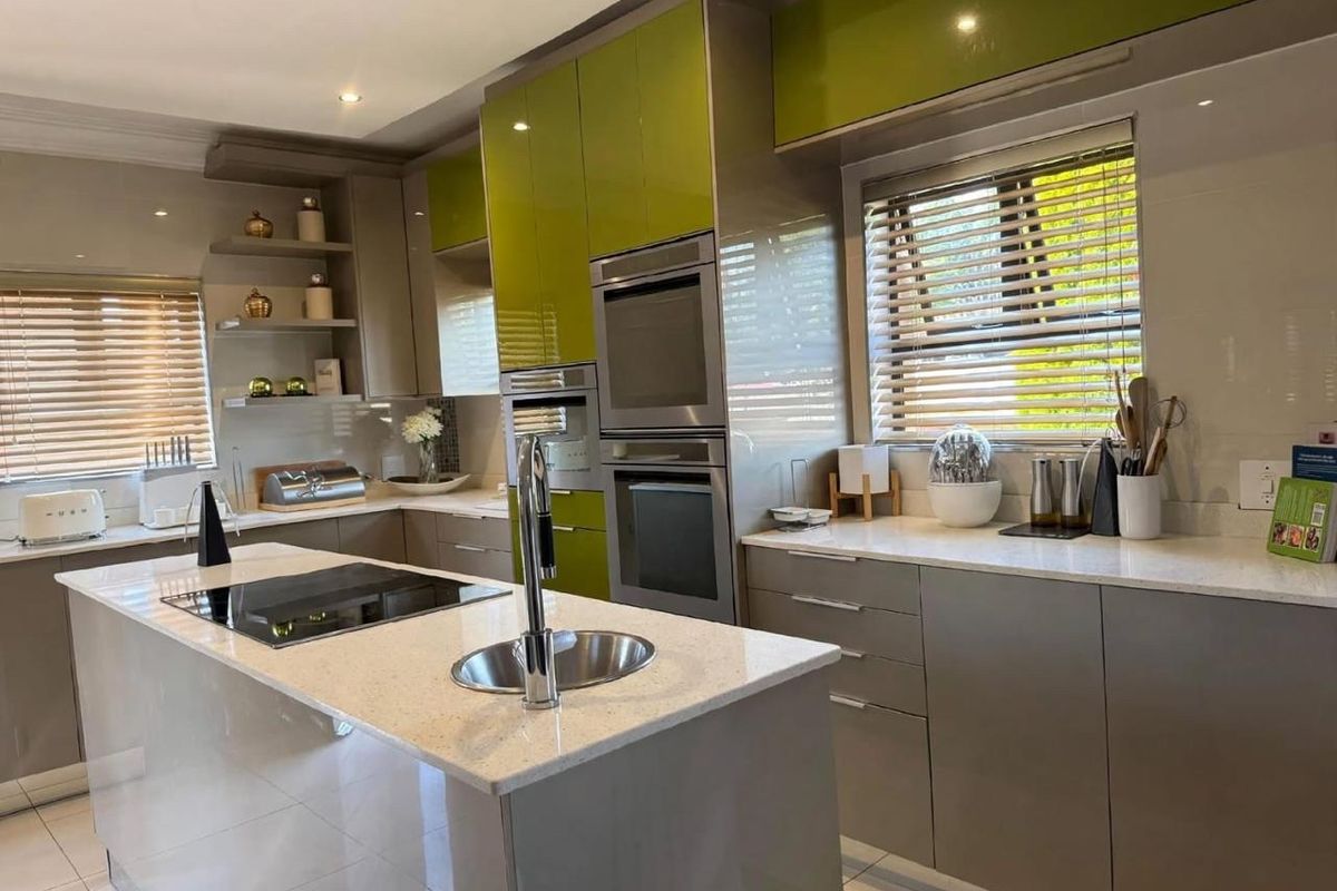Modern kitchen featuring high-gloss cabinetry, a central island with an induction hob and sink, built-in double ovens, and sleek quartz countertops.