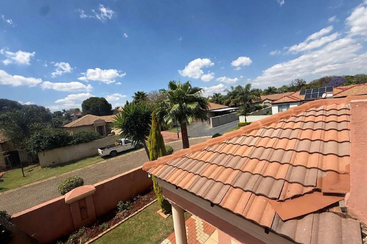 An elevated aerial view showing the property's tiled roof, surrounding garden, boundary wall, and the neighborhood street scene.