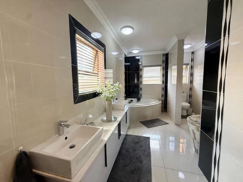 Modern bathroom featuring a double vanity with vessel sinks, a corner bathtub, and a separate toilet area with contemporary tiled finishes.