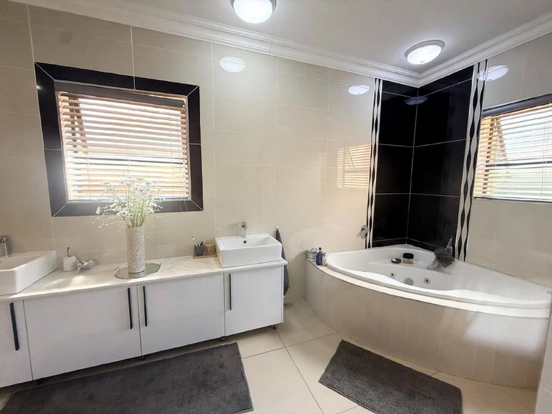 A well-maintained bathroom featuring a corner spa bath, dual vanity with ceramic basins, and modern tiled finishes throughout.