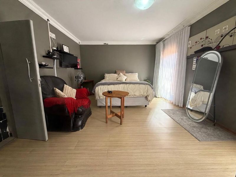 Spacious bedroom featuring light-toned laminate flooring, crown molding, and a large sliding glass door providing natural light.