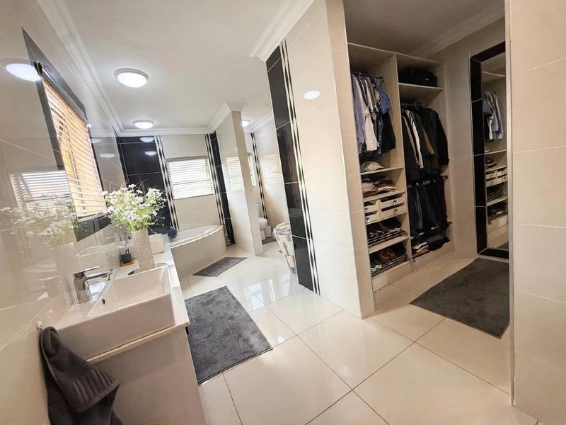Modern bathroom featuring a vessel sink vanity, corner bathtub, and integrated walk-in wardrobe with extensive built-in shelving and storage.