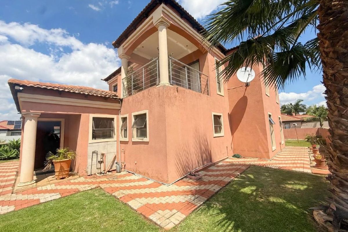 Rear view of a two-story house featuring a balcony with stainless steel balustrades, tiled roof, and a paved garden walkway.