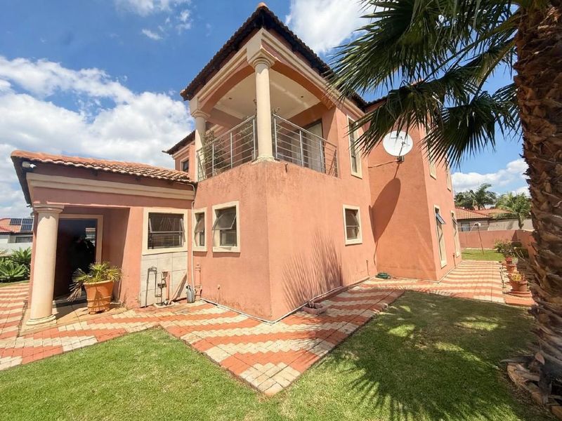 Rear view of a two-story house featuring a balcony with stainless steel balustrades, tiled roof, and a paved garden walkway.