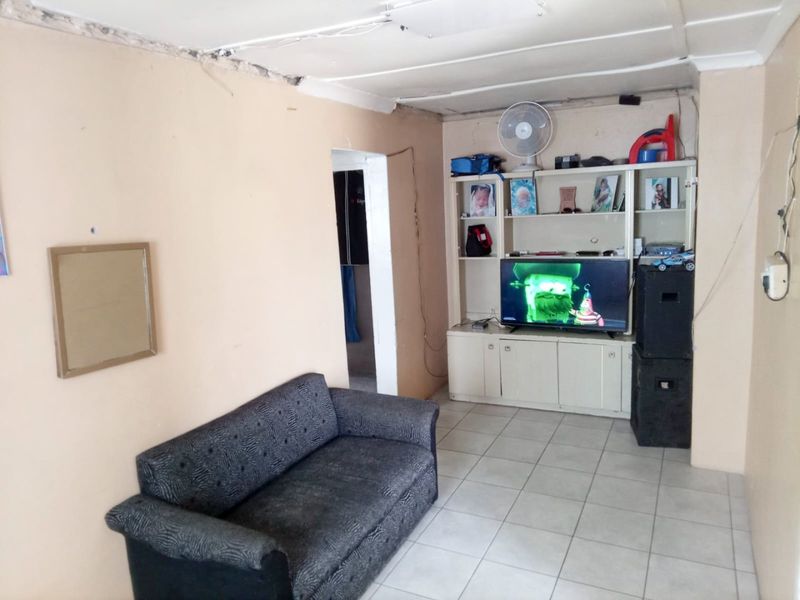 A living room featuring tiled flooring and a built-in wall unit, currently showing signs of wear and requiring maintenance to the ceiling and walls.